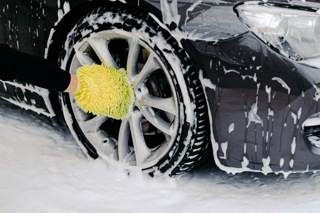 Workers hand with yellow sponge washing car wheels with detergent for cleaning vehicles